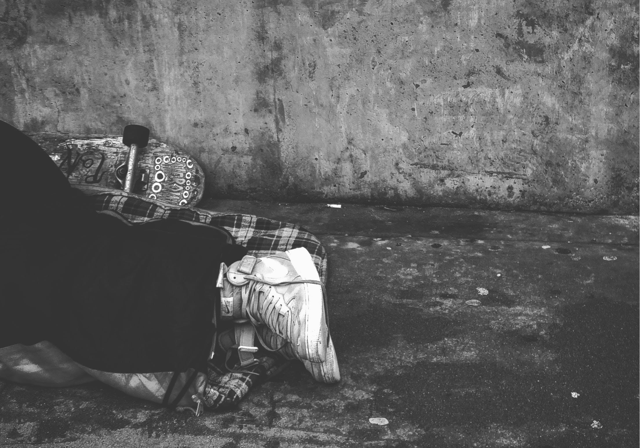 Navigating Grit in Homelessness Advocacy_B and W Photo of Homeless Youth Asleep on Ground with Skateboard next to his feet.