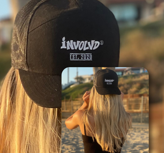 Person wearing a black cap with 'Involvd'\ branding on a beach